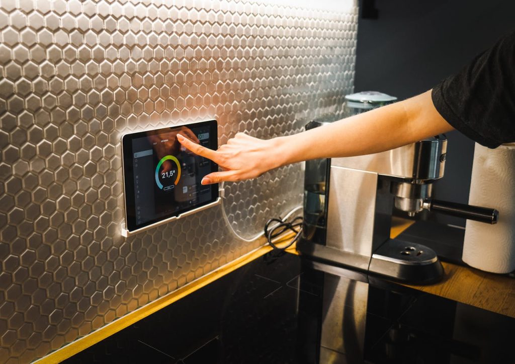 pexels-photo-16423103 Modern kitchen scene featuring a hand using a tablet to control a smart home system.